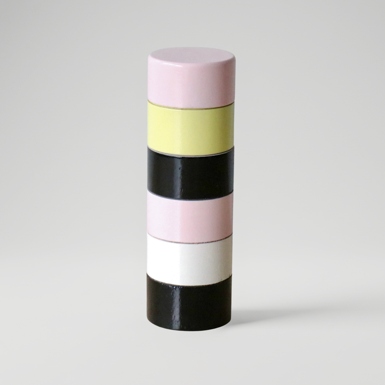 Cylindrical Semi D salt grinder with alternating pink, yellow, black, and white stripes on a gray background