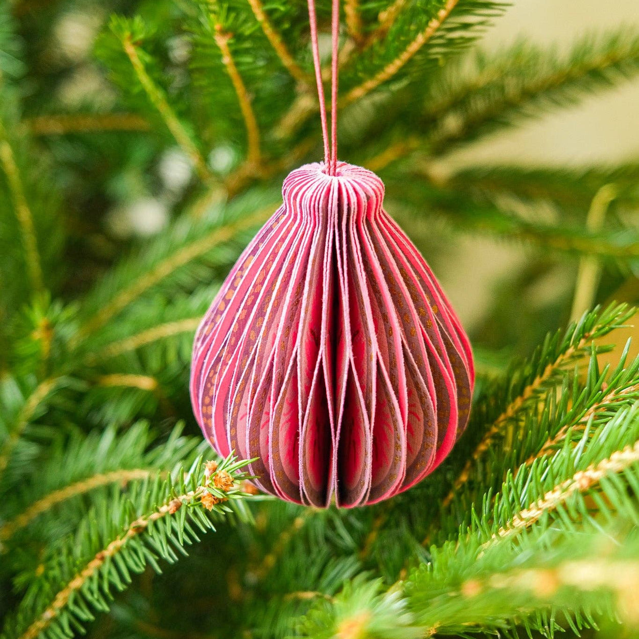 Pink paper ornament hanging on a green Christmas tree