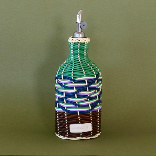 Decorative olive oil bottle with woven design and metallic nozzle on a green background.
