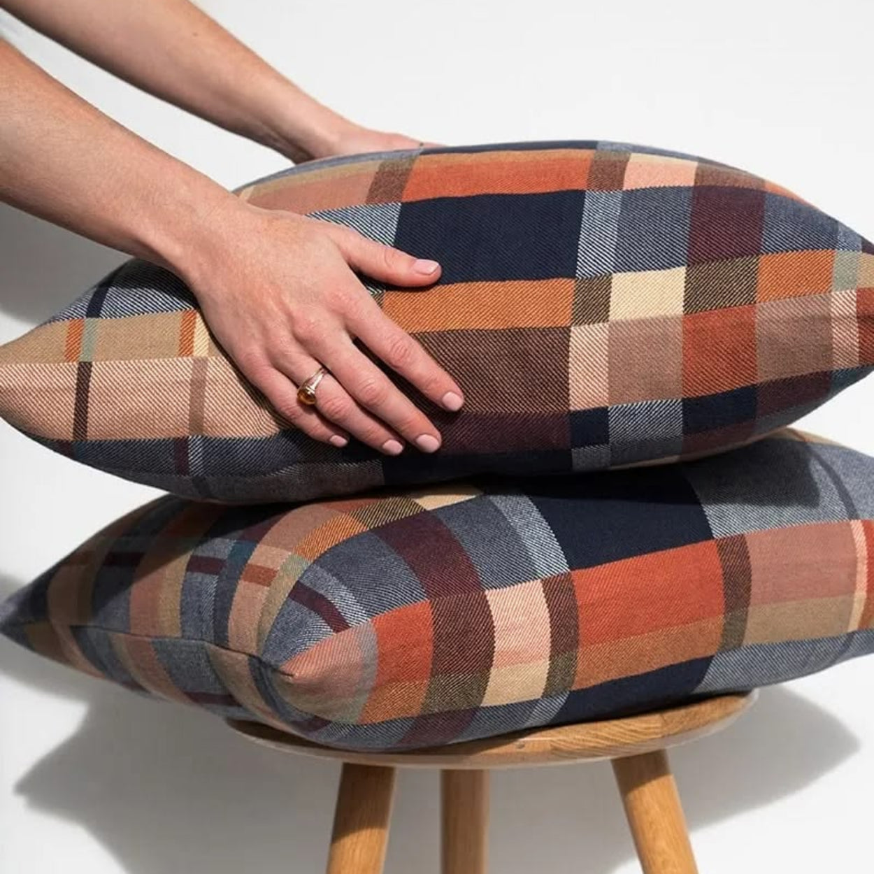 Stack of Mungo Karoo plaid double cotton patterned cushions on a wooden stool with a hand resting on top.