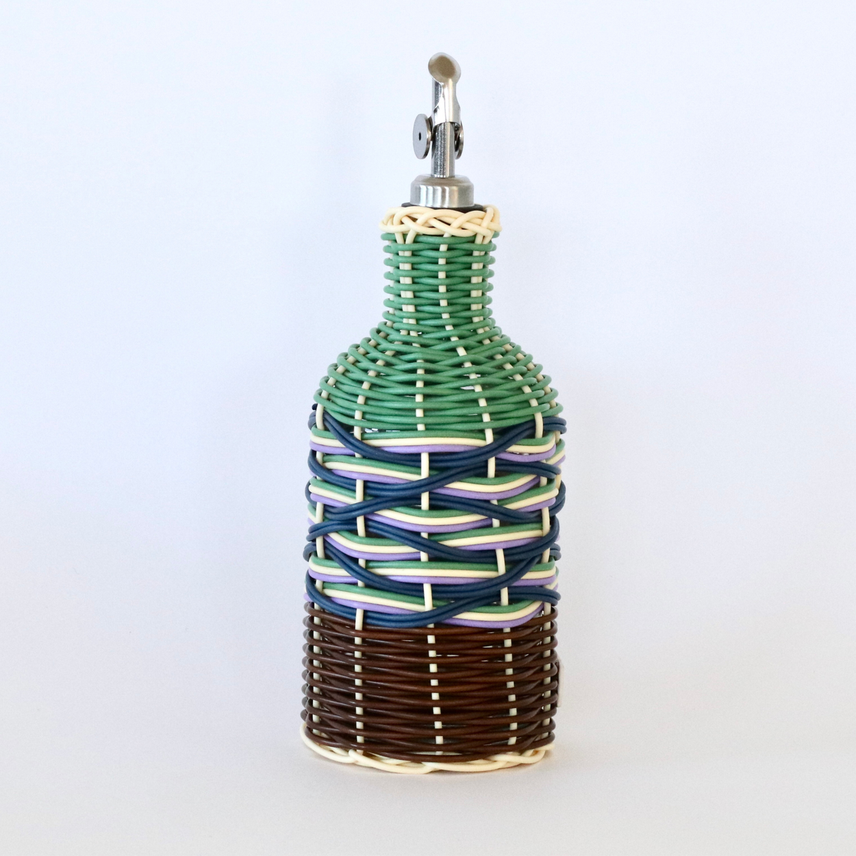 Decorative olive oil bottle with green, brown and navy woven design and metallic nozzle on a white background