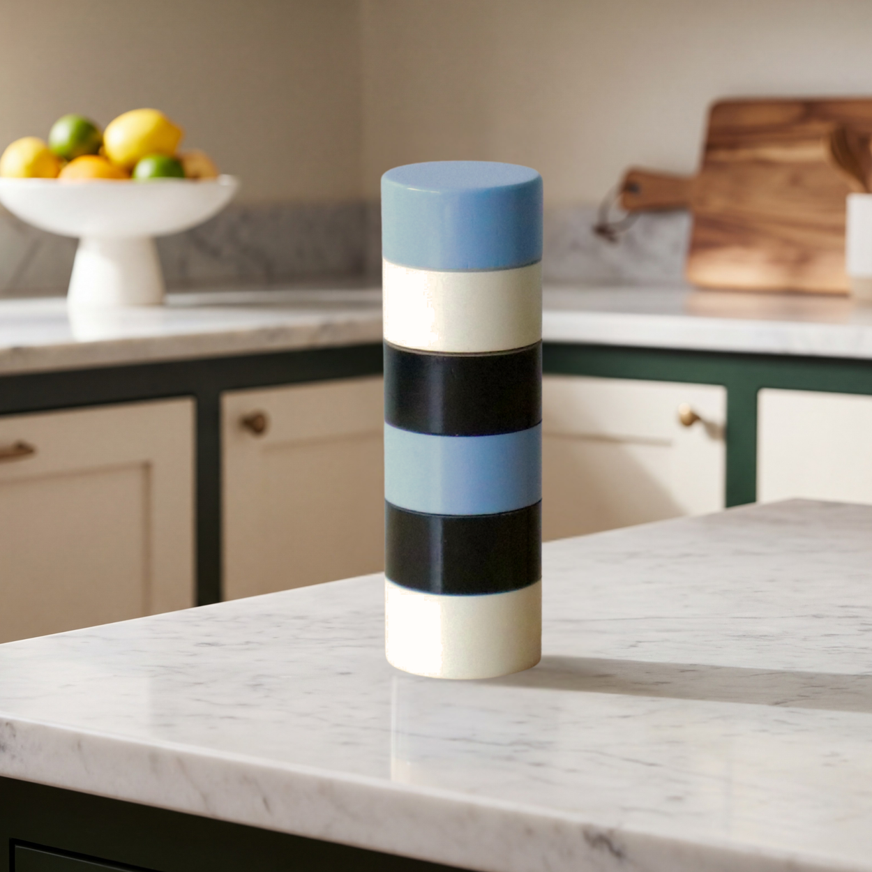 Colorful striped Semi D salt pepper grinder on a kitchen counter with fruit and cutting board in the background 