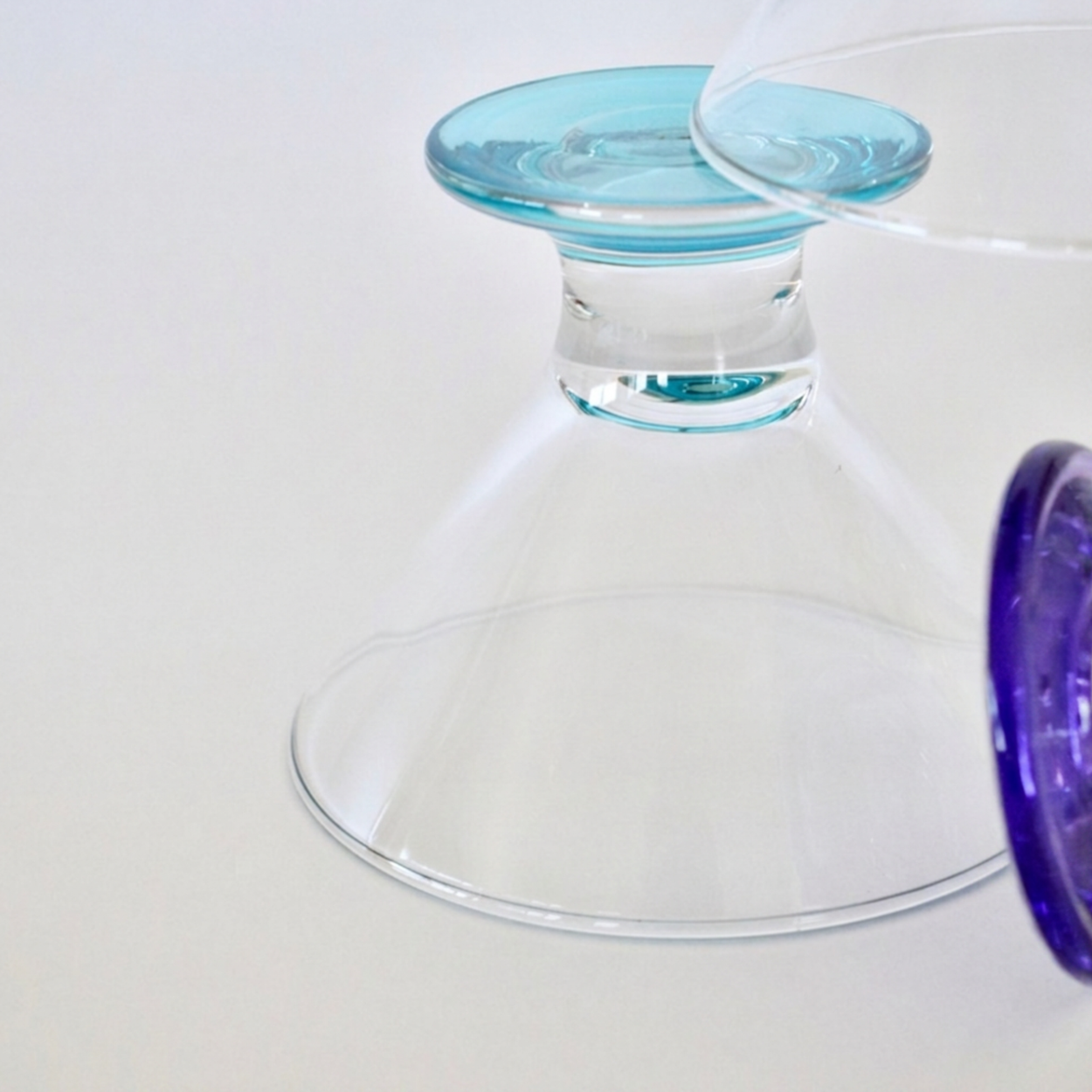 Clear glass martini glasses with blue and purple bases on a white background