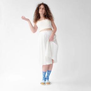 Woman in white pleat skirt wearing Bonne Maison pale blue polka dot socks on white backdrop.