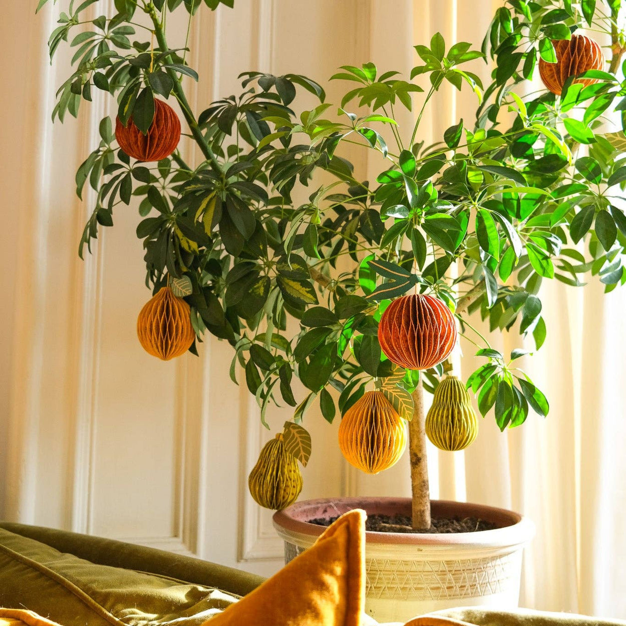 Potted plant with decorative paper lanterns in a room with a couch and pillows.