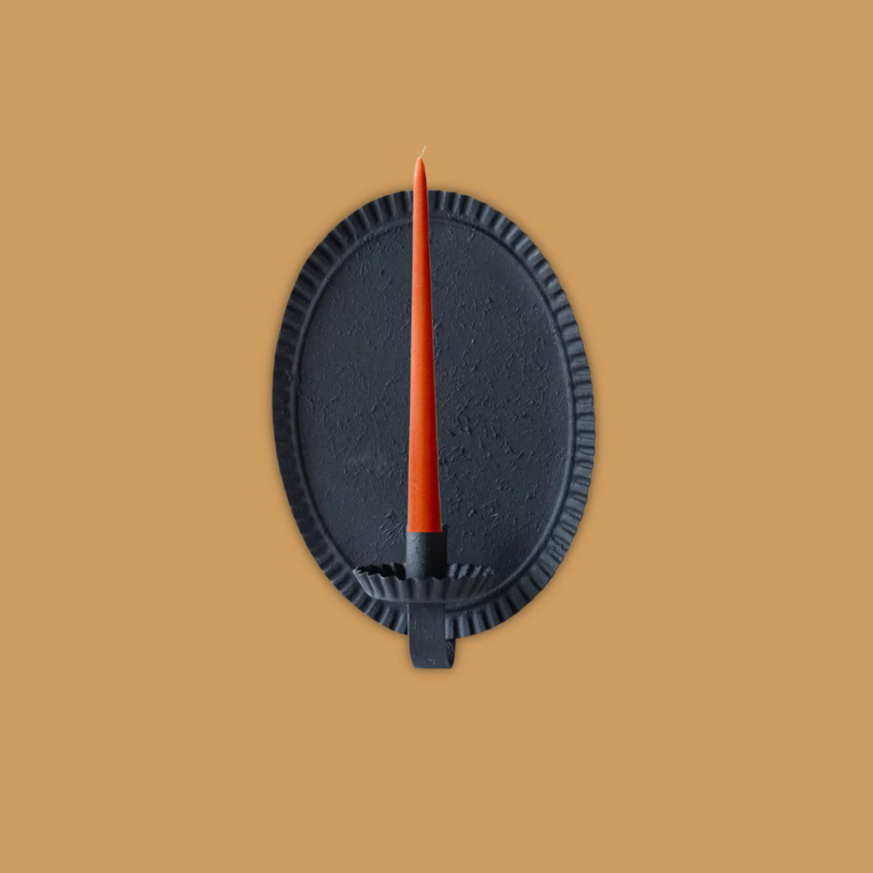 Blackoval candle sconce with an orange candle on a soft terracotta background