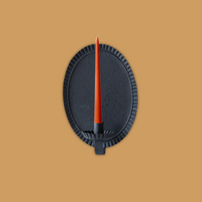 Blackoval candle sconce with an orange candle on a soft terracotta background