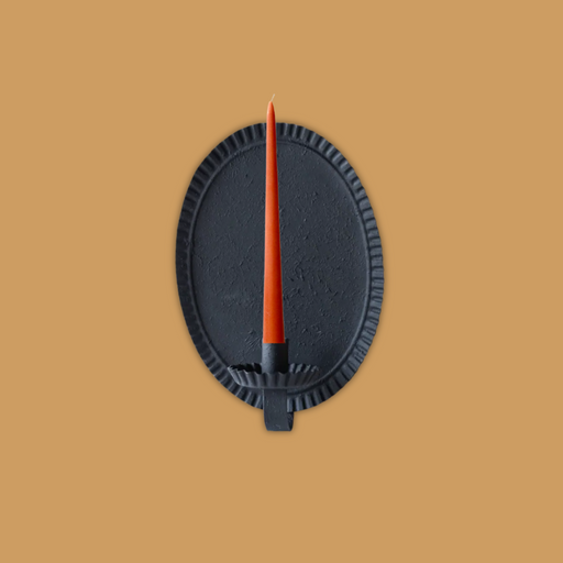 Blackoval candle sconce with an orange candle on a soft terracotta background