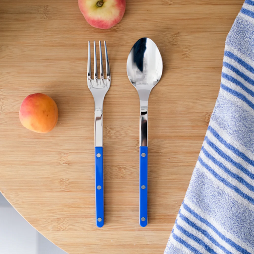 Silver fork and spoon with blue handles on a wooden surface with fruits and a towel.