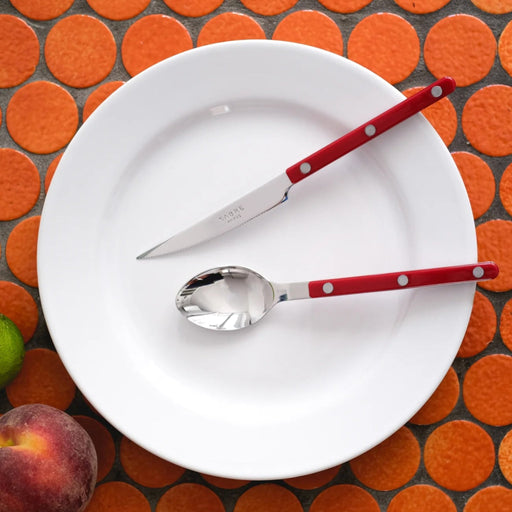 Sabre Paris Burgundy 4 piece flatware set, on orange tile tabletop.