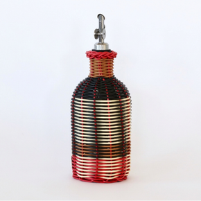 Decorative olive oil bottle with black, red and cream woven design and metallic nozzle on a white background