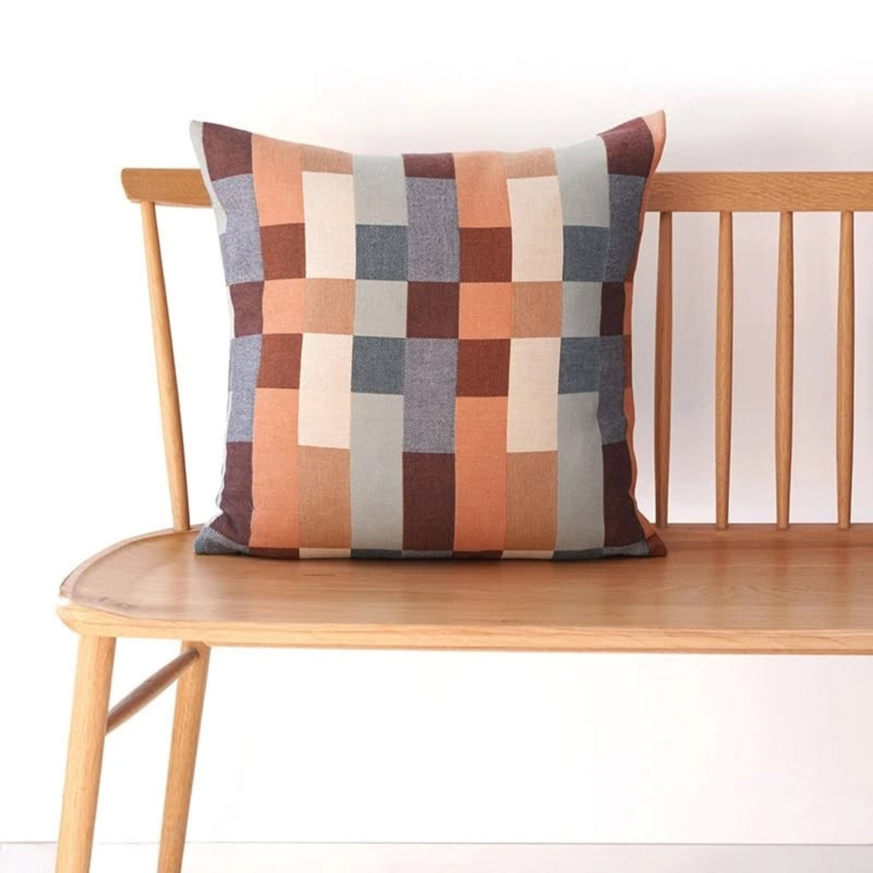 Mungo Wild Fire Multicolored checkered double cotton pillow on a wooden bench against a white background