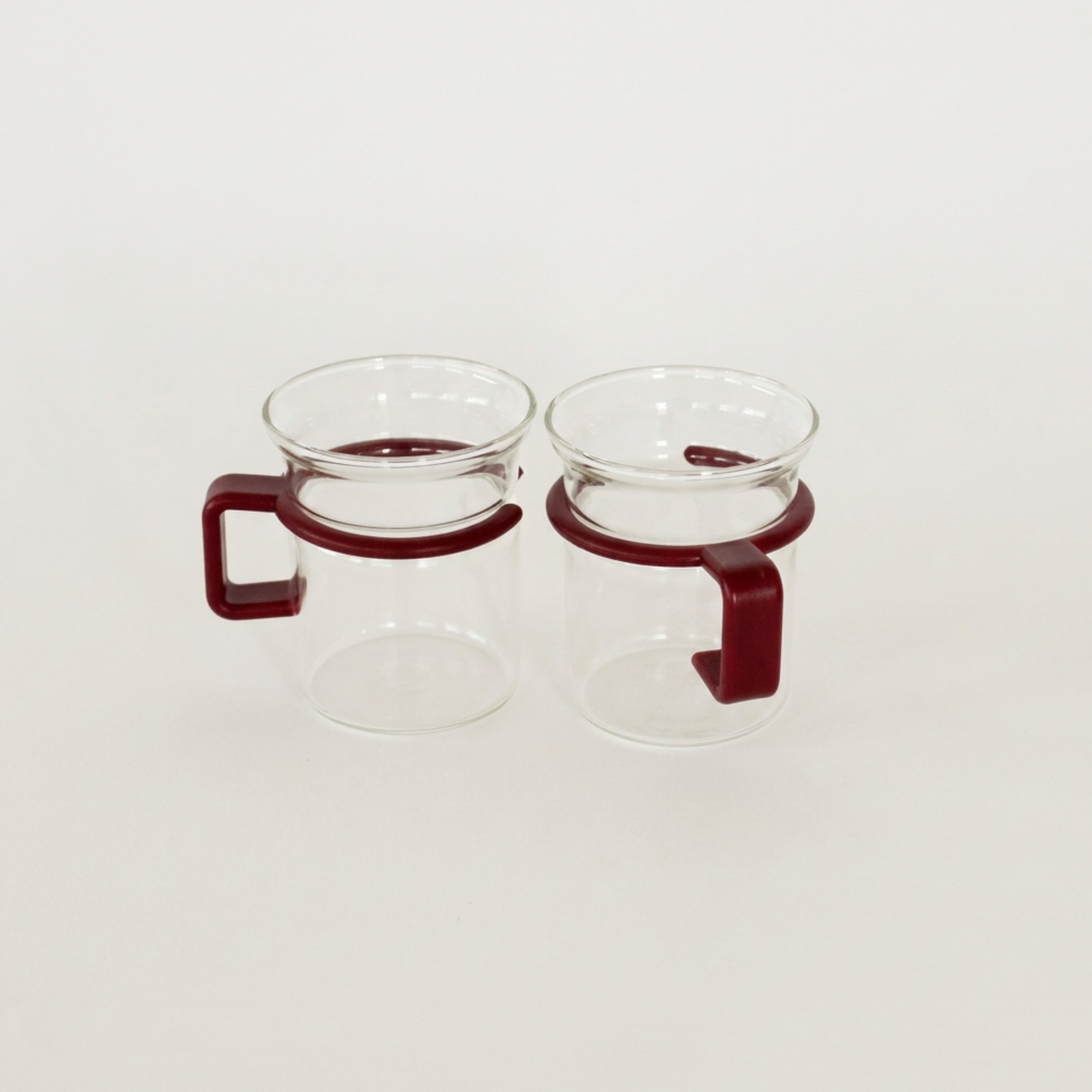 Two clear glass cups with red holders on a white background