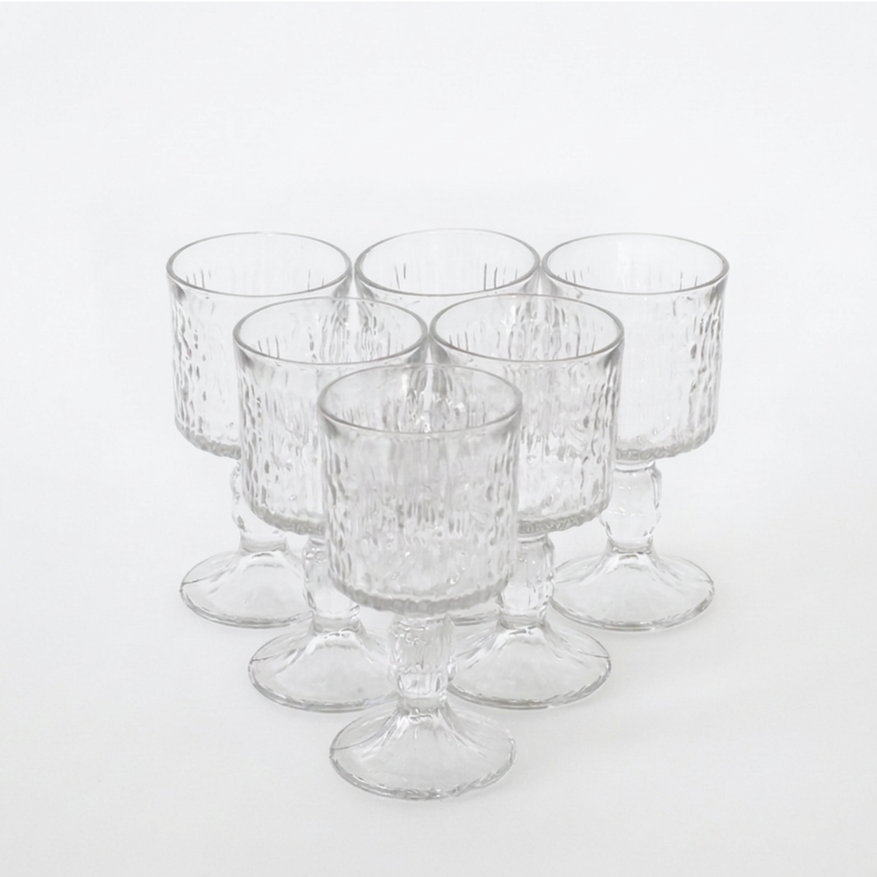 Six clear textured glass candleholders with pedestal bases, arranged in a cluster on a white background.