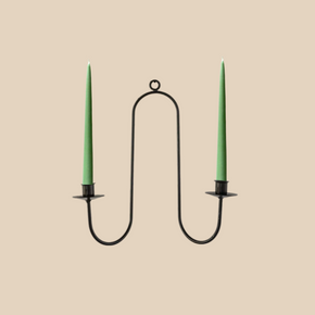 Black metal candle holder with two green candles on a beige background