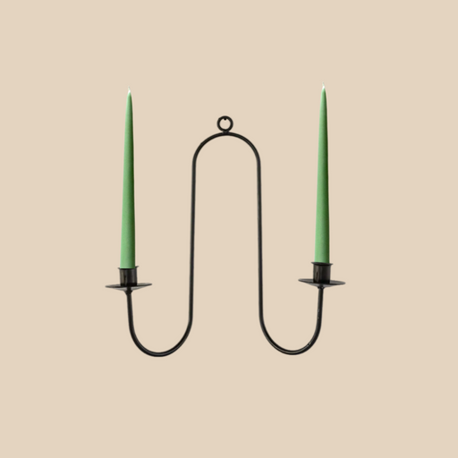 Black metal candle holder with two green candles on a beige background
