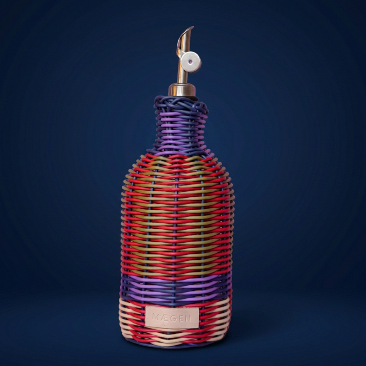A woven bottle cover or decorative bottle wrap in a multicolour wicker pattern with purple, red, orange, green, and cream stripes, featuring a silver-toned pour spout and a small beige brand patch that reads 'MAEGEN'.