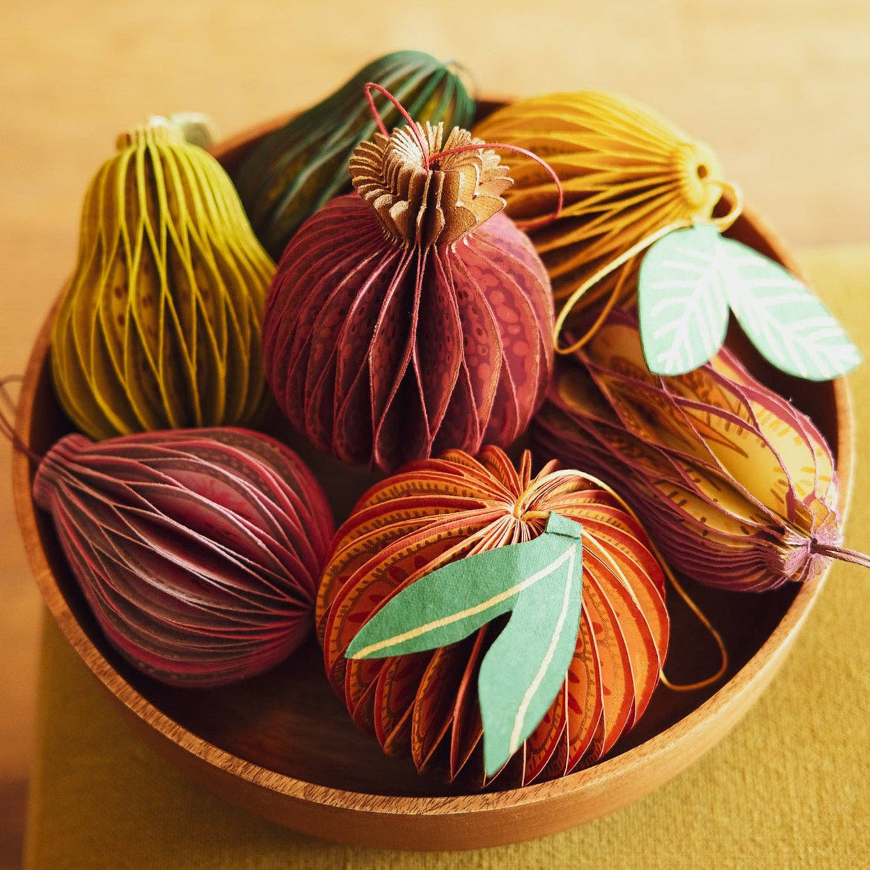 Decorative paper fruits in a wooden bowl on a wooden surface