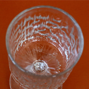 A close-up top-down view of a clear textured glass tumbler on a solid orange background.