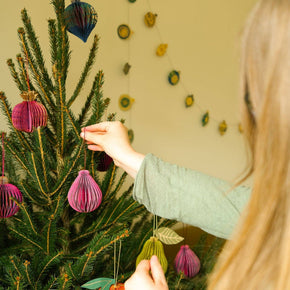 Person decorating a Christmas tree with colorful ornaments in a cozy room.