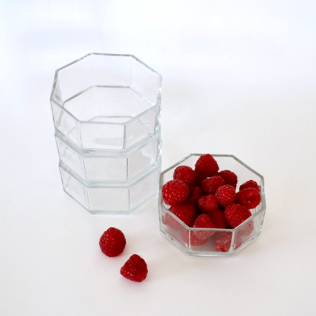 Octagonal glass containers with raspberries on a white background