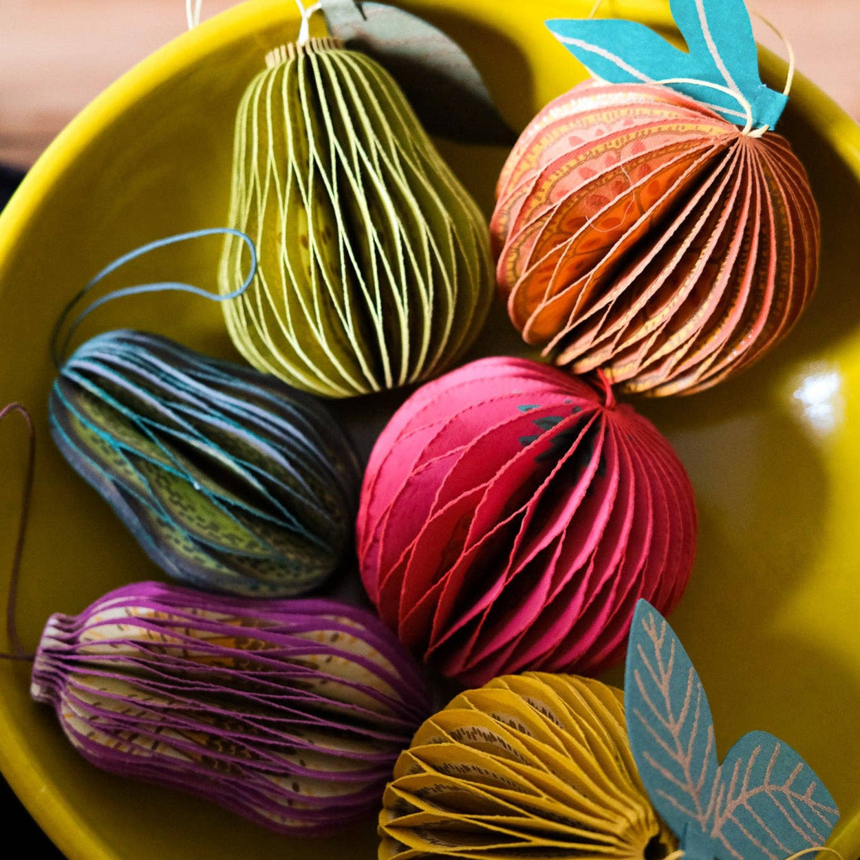 Colorful paper ornaments with leaf accents in a yellow bowl.