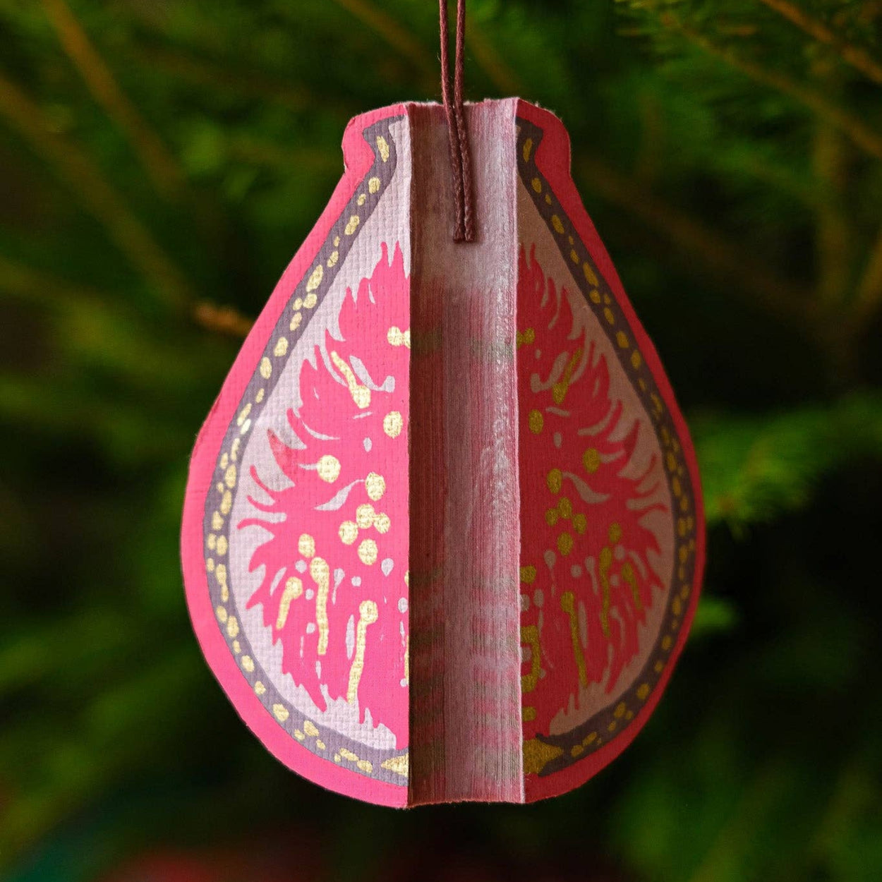 Decorative pink teardrop ornament with intricate patterns hanging against a green foliage background.