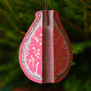 Decorative pink teardrop ornament with intricate patterns hanging against a green foliage background.
