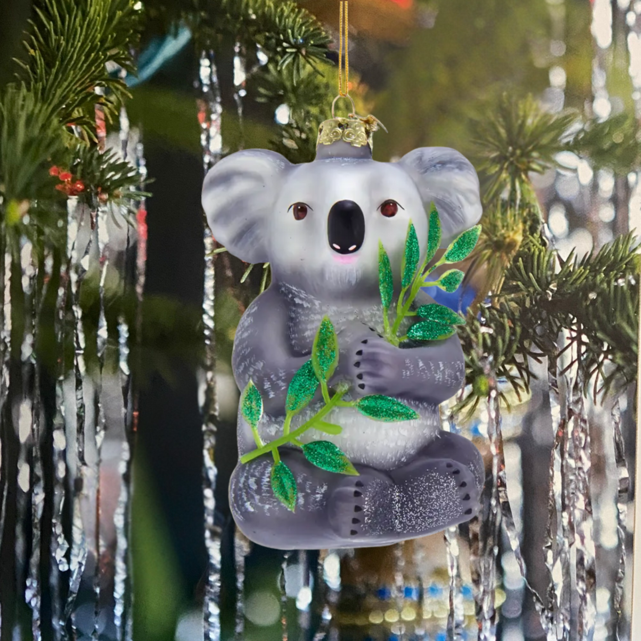 Decorative koala ornament hanging on a tree with green leaves.
