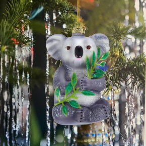 Decorative koala ornament hanging on a tree with green leaves.