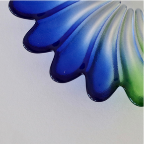 A close-up of a glossy, scalloped decorative object in deep blue with a green gradient section, shown against a plain light background.