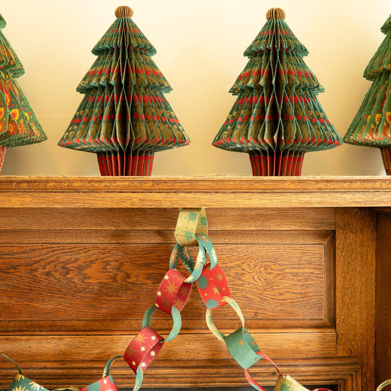 Decorative paper Christmas trees on a mantelpiece with a paper chain.