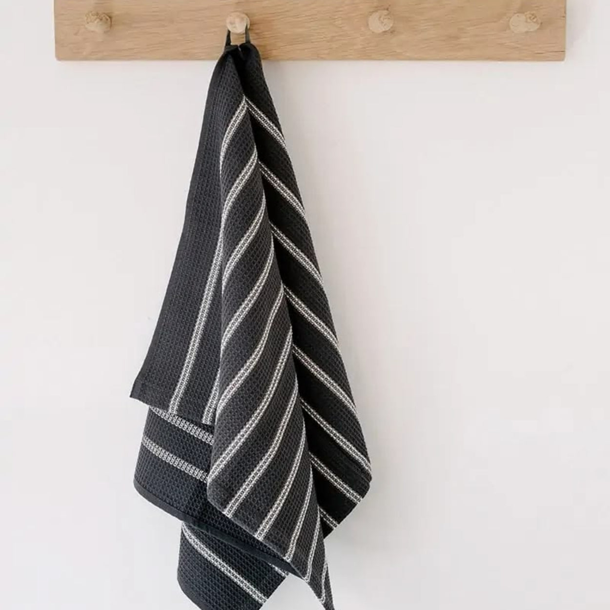 Black and white striped towel hanging on a wooden rack against a white wall.