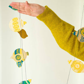 Decorative string with colorful fish-shaped ornaments held by a hand wearing a yellow sweater.