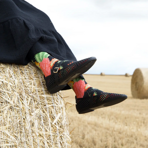 Woman on hay bale with black skirt and shoes and Bonne Maison pineapple socks.