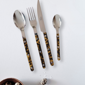 Set of cutlery with tortoiseshell handles on a white surface with a bowl of quail eggs and a striped cloth.