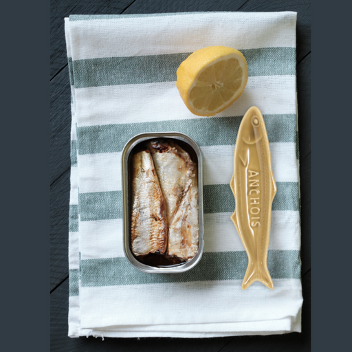 Sardine can with a lemon and a decorative fish-shaped dish on a striped cloth.
