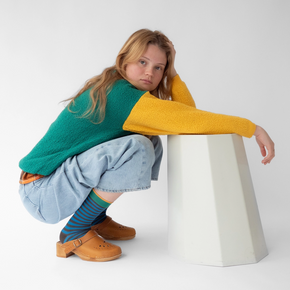 Woman in greens and green and yellow sweater wearing Bonne Maison Blue Black Stripe socks against a white backdrop.