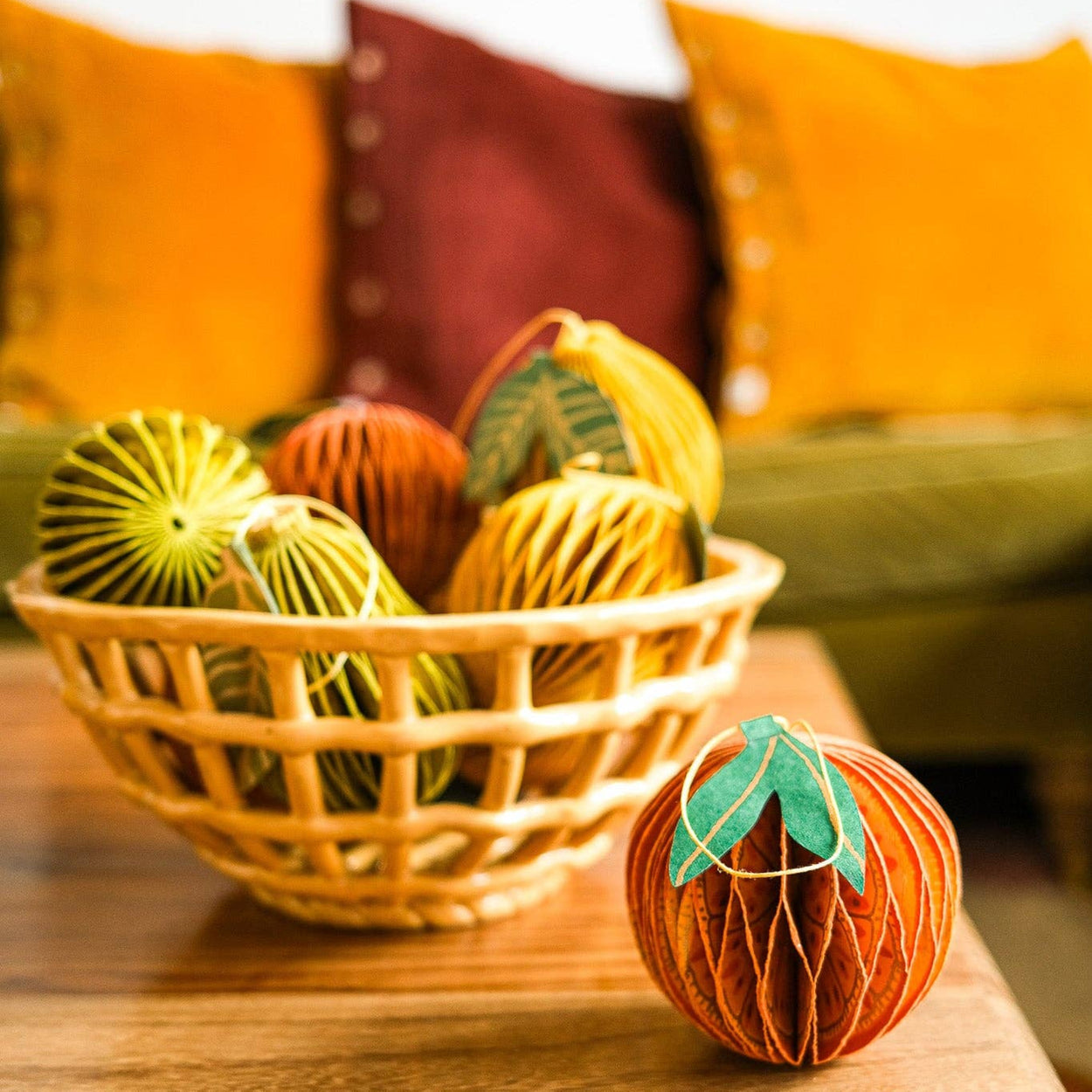 Decorative paper pumpkins in a basket on a wooden table with a blurred background