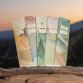 Set of Juniper Ridge Incense packets on a wooden branch with a blurred landscape background