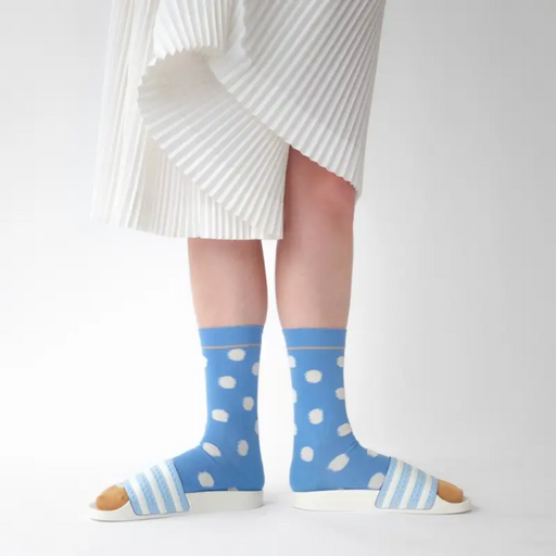 Woman in white pleat skirt wearing Bonne Maison pale blue polka dot socks on white backdrop.