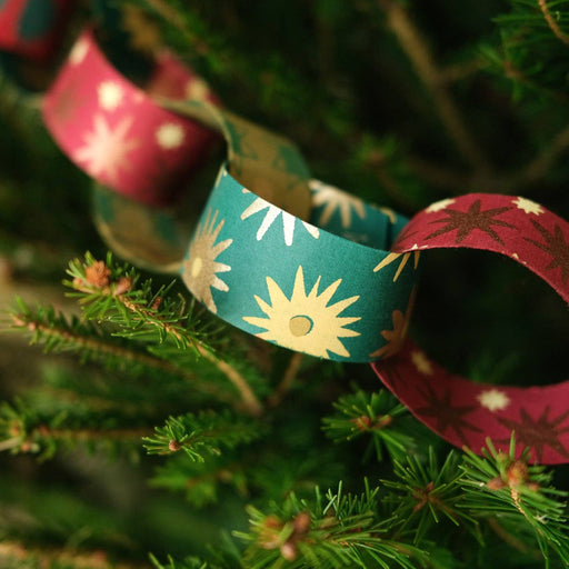 Decorative paper chains with sun and star patterns hanging on a Christmas tree.