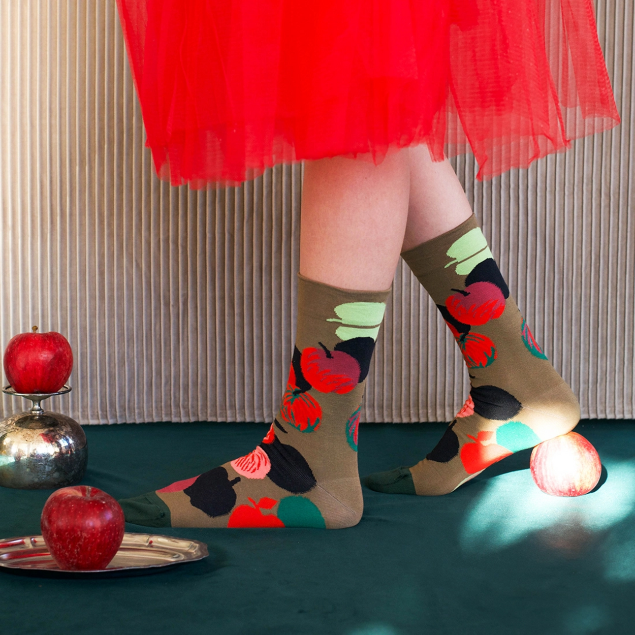 Woman in red skirt wearing Bonne Maison Apples socks  against green and beige backdrop.