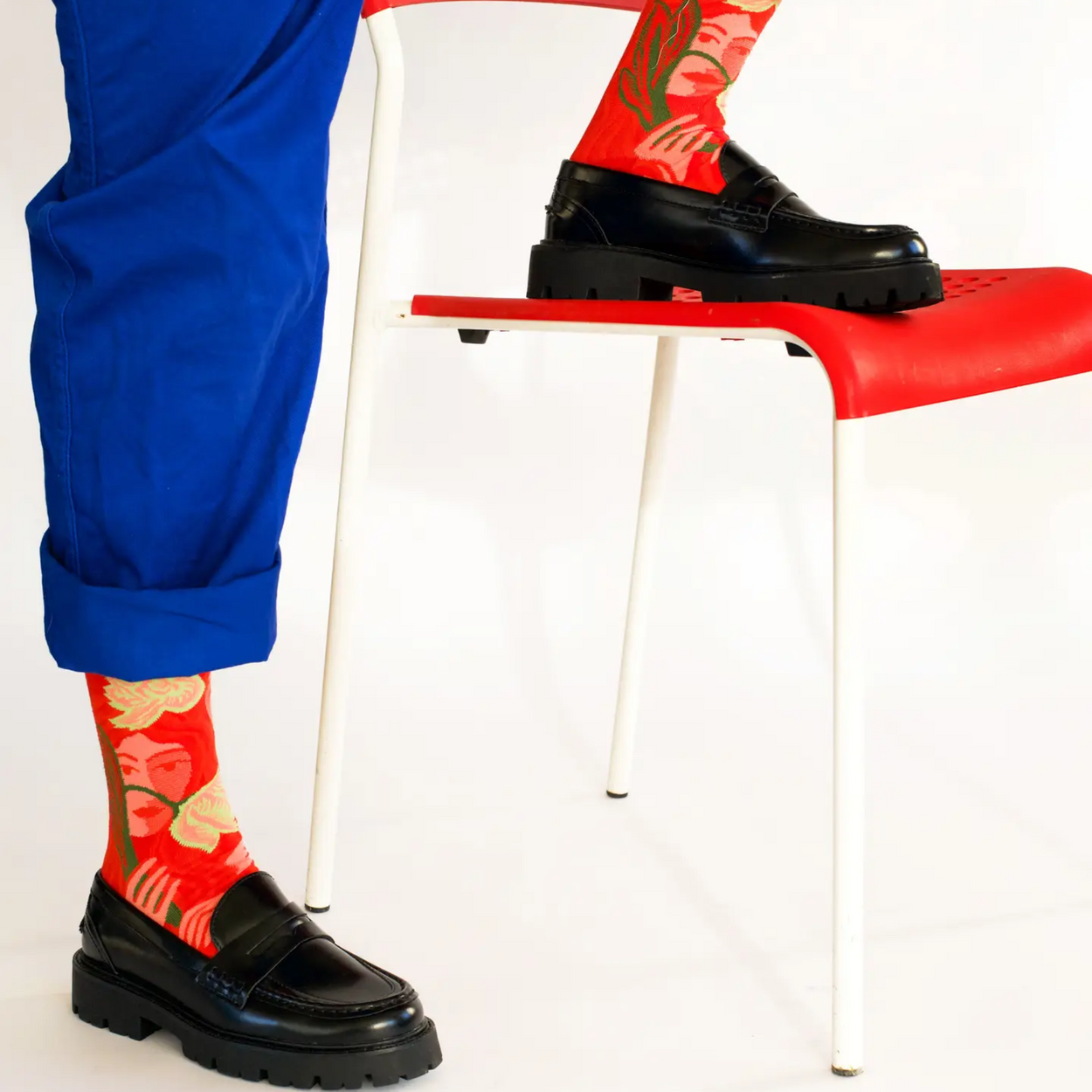Person with blue pants wearing Bonne Maison red visage socks with foot on red chair