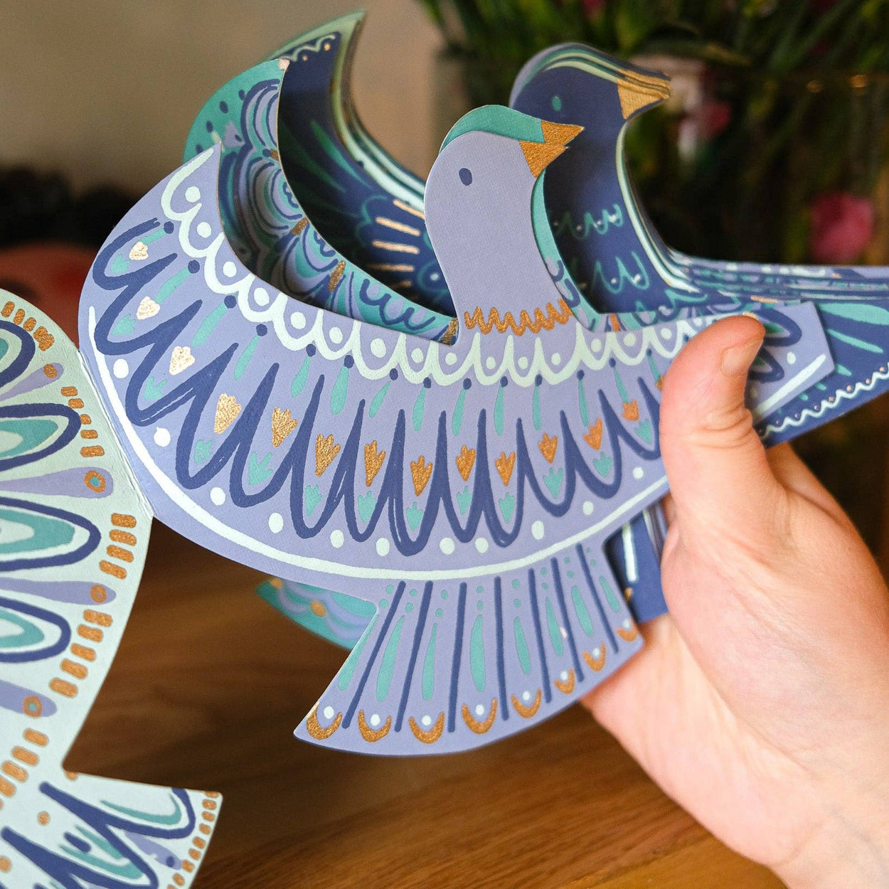 Colorful paper cutout of a dove held by a hand with flowers in the background