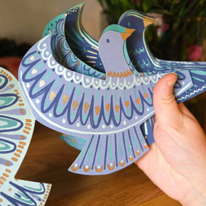 Colorful paper cutout of a dove held by a hand with flowers in the background