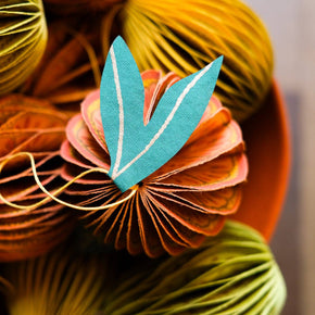 Decorative paper fruit with a central blue leaf-shape on a blurred background