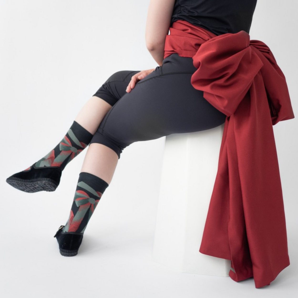Woman in black leggings with red sash wearing Bonne Maison Ribbon socks on white backdrop.