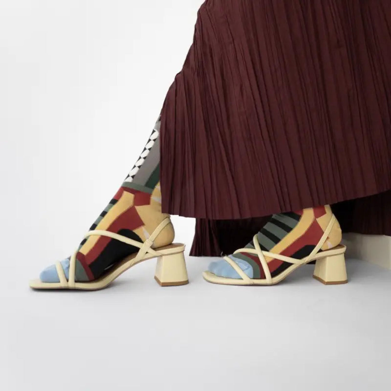 Bonne Maison Colourful geometric-patterned sandals worn with a pleated skirt on a light background