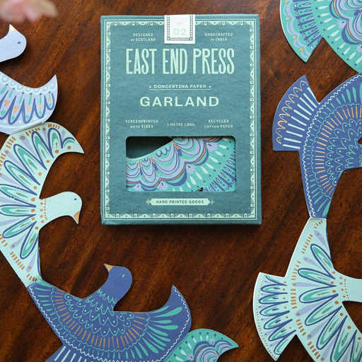 Pack of 'East End Press Garland' on a wooden surface with decorative cutouts.